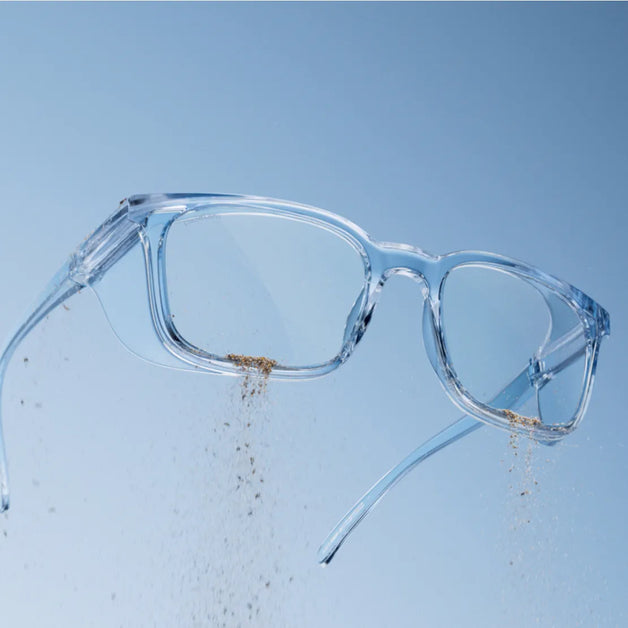 Clear blue-tinted eyeglasses from Stoggles with dust particles falling off the frame against a blue background.