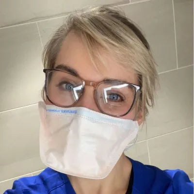 Healthcare worker in blue scrubs and a mask wearing clear Stoggles safety glasses.