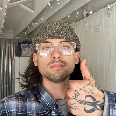 Person in Stoggles and a beanie, wearing a plaid shirt, posing indoors with a thumbs up.