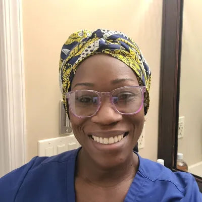Woman wearing Stoggles and patterned head wrap smiling at camera indoors.