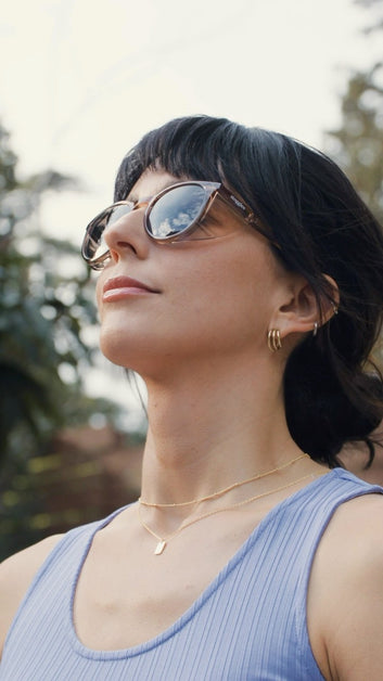 Woman in a blue dress wearing Stoggles sunglasses, looking up toward the sky on a bright day.