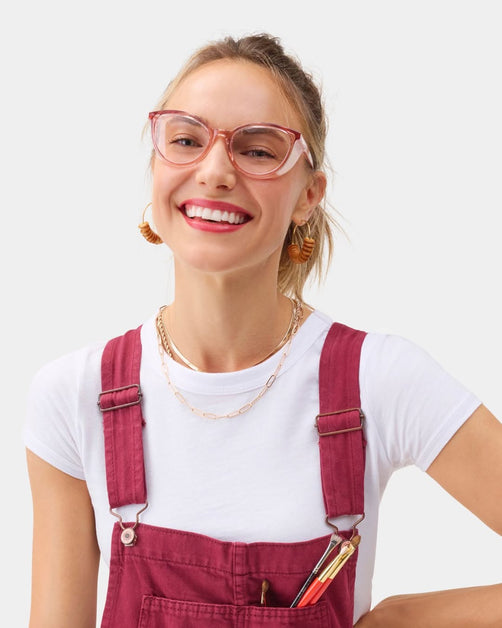 Smiling woman in pink overalls wearing matching pink cat-eye Stoggles glasses.